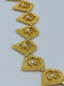 Detail view of the belt body showing a row of hinged open-lattice filigree heart medallions with beaded borders and white bead centers in warm gold-tone