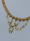 Angled close-up of the front V-drape showing raised radial sunburst flower medallions with white bead centers and cascading multi-strand coin disc drop chains