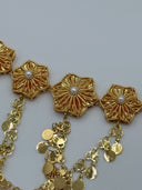 Macro close-up of two raised radial sunburst flower medallions showing the detailed petal cutwork, white bead centers, and multi-strand coin disc drop chain attachments