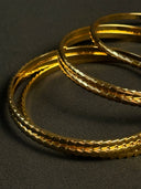 Three gold bangles on a dark gray background