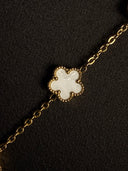 Gold bracelet with a white clover-shaped charm on a black background