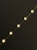 Gold necklace with white flower-shaped pendants on a black background