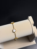 Gold bracelet with a flower design on a white stand against a dark background