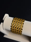 Gold bracelet on a white stand against a black background