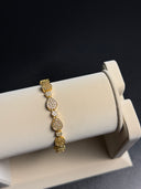 Gold bracelet on a white jewelry display stand with a black background