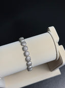 Silver bracelet on a white cylindrical stand with a dark background