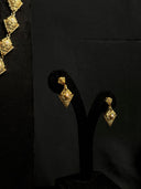 Gold-tone diamond tile drop earrings on a black earring stand, each featuring two stacked engraved tiles with a pearl-like centre bead