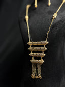 Close-up of gold-tone stacked bar pendant necklace showing four textured cylindrical bars in descending size with pointed ends and chain tassel fringe