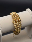 Three gold-tone diamond-cut bead stacking bracelets displayed on a white jewellery roll, front view
