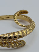Full view of gold-tone Serpenti-inspired hinged bangle with pavé crystal scale body and coiled serpent head terminal on white background