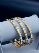 Set of 3 gold-tone rigid bangles with rigato engraved surface and raised floral motifs displayed on white jewelry stand