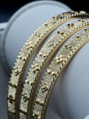 Macro detail of gold-tone rigato bangle set showing engraved surface texture, clover motifs, and milgrain edge border
