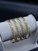 Set of four gold-tone wheat leaf interlocking bangles stacked on a white jewelry display roll against a dark background