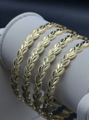Angled view of four Laurea wheat leaf bangles stacked on a white display roll, highlighting the layered stacking effect and leaf texture detail