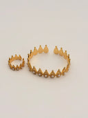 Gold-tone crown arch bangle and matching ring set with pearl accents and filigree texture, styled on a warm beige surface