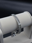 Silver-tone wide open-cuff bangle with Cannage diamond quilted lattice pattern displayed on a white jewelry roll against a dark background
