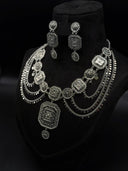 Oxidized silver-tone Turath collar necklace and matching drop earrings displayed on a dark bust, showing alternating round and square filigree medallions with coin disc swag chains