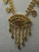 Close-up of the eye-shaped filigree pendant showing colored stone accents in red and green, intricate beaded border, and multi-strand teardrop tassel drop in gold tone