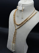 Full view of a 2-piece gold-tone jewelry set on a bust display, showing a double-strand textured bead lariat with pearl-finish tassel drop and matching long tassel drop earrings