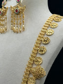 Angled side view of the full crescent bib pendant on a display stand showing layered filigree tiers, fuchsia stone accents, and dense cascading tassel fringe
