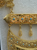 Detail of the crescent bib pendant showing open arabesque filigree scrollwork, pear-shaped fuchsia stone accents with turquoise-color bead halos, and cascading flower-link tassel fringe