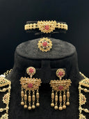 Close-up of a gold-tone maang tikka with a triangular open filigree pendant, white and pink stone accents, a horizontal ball chain bar, and three hanging star-burst medallion drops