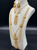 Full view of a gold-tone multi-strand filigree medallion necklace and earring set on a white bust against a dark background, showing layered ball-link chains, round filigree stations, and bead tassel drops