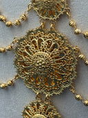 Macro detail of a single large open filigree medallion station showing the intricate scrollwork, granulated bead border, and central floral motif in gold tone