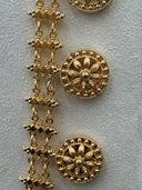 Macro detail of the coin chain side strand showing engraved round medallion discs with petal and spoke motifs connected by cross-link chain segments in gold tone