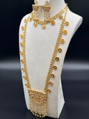 Full view of a Khaleeji-style gold-tone jewelry set on a white bust against a dark background, showing a wide multi-row coin chain choker and a long opera-length coin chain necklace with a large half-moon filigree pendant, paired with matching chandelier earrings