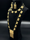Full view of a Khaleeji-style gold-tone jewelry set on a black bust showing a shorter square plaque collarbone necklace layered over a long opera-length necklace with a large rectangular pendant and bead tassel fringe, paired with matching drop earrings