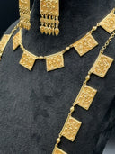 Detail shot of both necklaces on a black bust showing the engraved square plaques with raised floral and geometric center motifs and beaded border edges, connected by faceted bead links on a fine chain