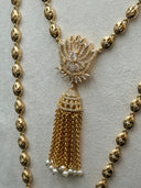 Detail of the shorter necklace showing the engraved oval bead chain and the smaller lotus pendant with pave stone detailing, jhumka bell cap, and a single chain tassel drop with white bead finish
