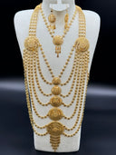 Full view of a Khaleeji-style gold-tone set on a white bust against a dark background, showing a wide multi-strand clover-link necklace with five graduated sunburst filigree medallions and matching drop earrings
