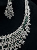 Close-up of the bib necklace and one chandelier earring showing emerald-green rectangular halo stones, marquise clear stones, and leaf spray drops