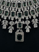 Macro close-up of the bib necklace body showing rows of emerald-green rectangular stones in pavé halo frames with marquise and pear-cut clear stone separators and double rectangular pendant drop at center