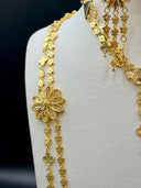 Close-up of a single large filigree daisy station on the long necklace showing open petal construction, engraved leaf detailing, and three-strand clover tassel drop
