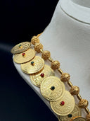 Close-up of the necklace showing engraved coin discs with red and green stones and textured filigree ball spacers