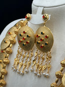 Detail of the necklace chain showing engraved coin discs with red and green stones and textured filigree ball spacers on a light background